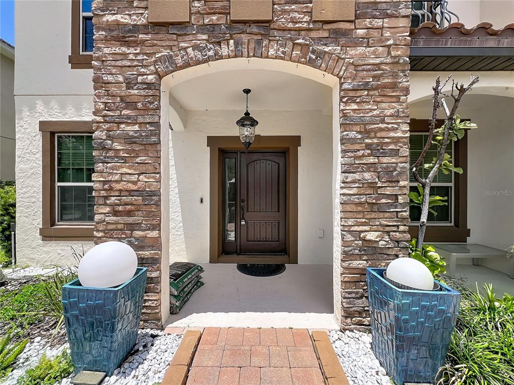 The front entrance features a stone-faced archway, a dark wood door, and two blue planters — 8316 LOOKOUT POINTE DRIVE, WINDERMERE, FL
