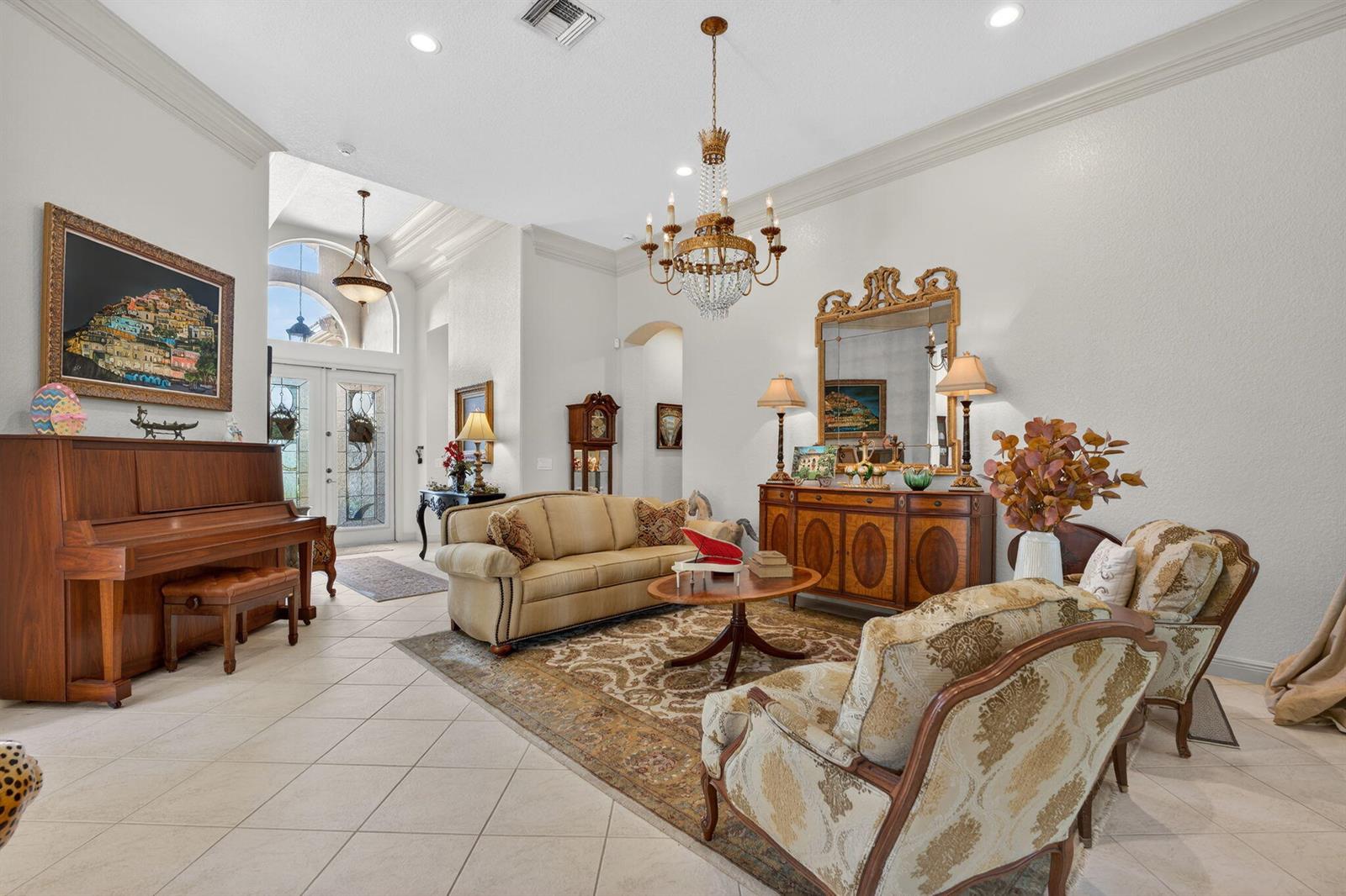 A formal living room features a piano, chandelier, area rug, and traditional furniture on tile — 7741 NW 120th Drive, Parkland FL 33076, PARKLAND, FL