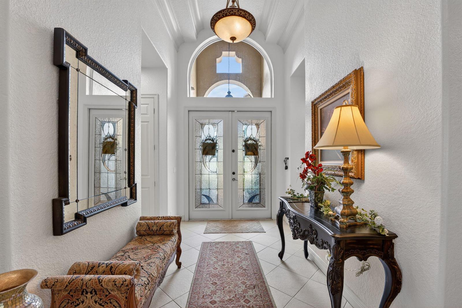 A bright entryway features a tiled floor, a patterned bench, a console table, and double doors — 7741 NW 120th Drive, Parkland FL 33076, PARKLAND, FL