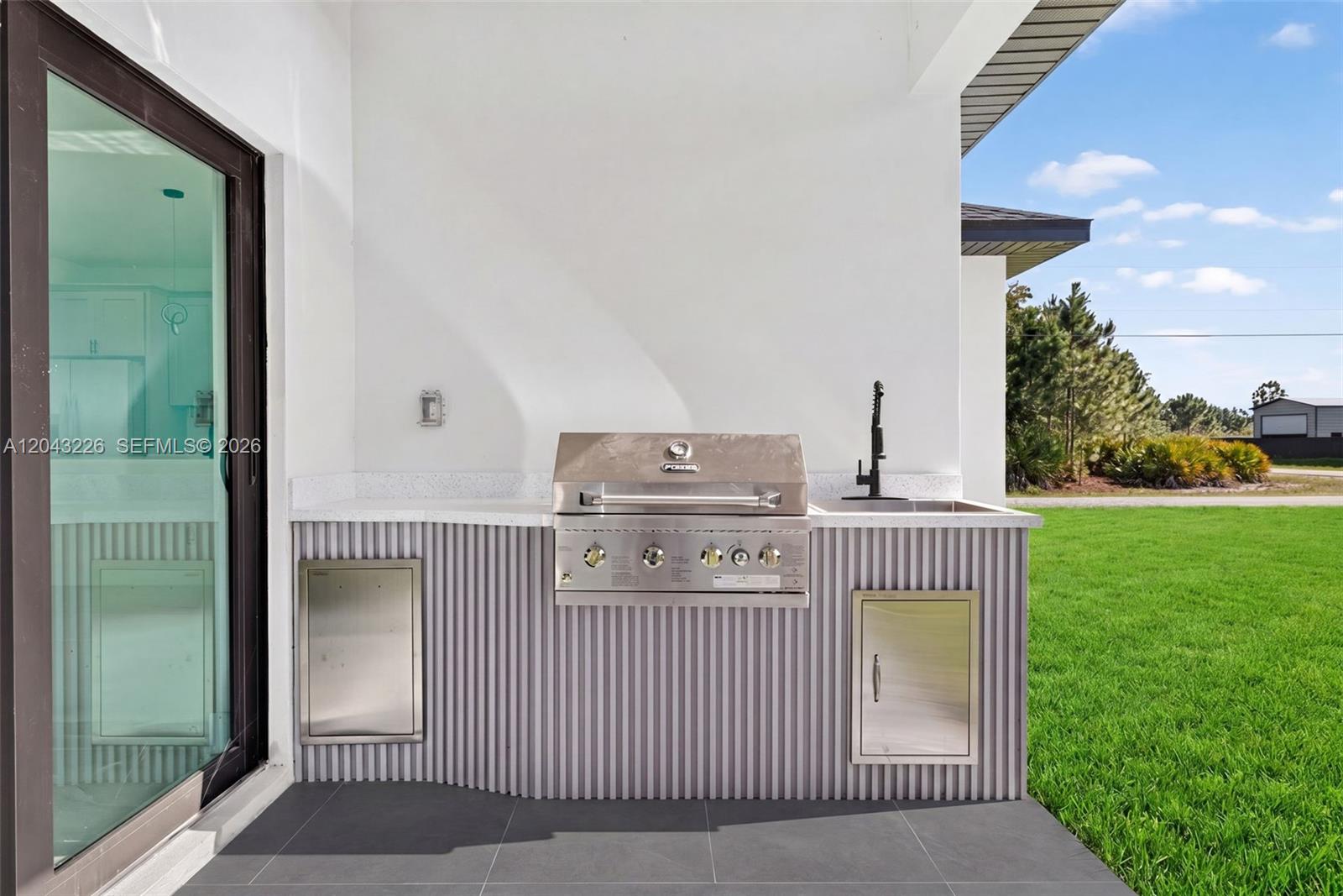 An outdoor kitchen features a stainless steel grill, sink, and corrugated siding on a patio — 3706 N Gene Ave, Lehigh Acres FL 33971, LEHIGH ACRES, FL