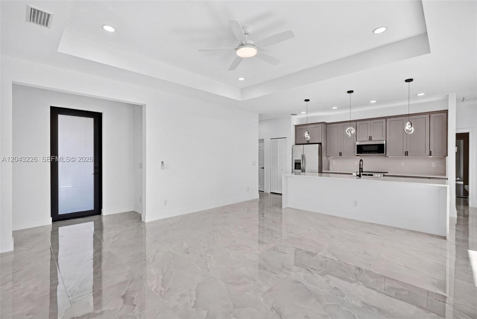 This open-concept kitchen and living area features white walls, tile flooring, and gray cabinetry — 3706 N Gene Ave, Lehigh Acres FL 33971, LEHIGH ACRES, FL