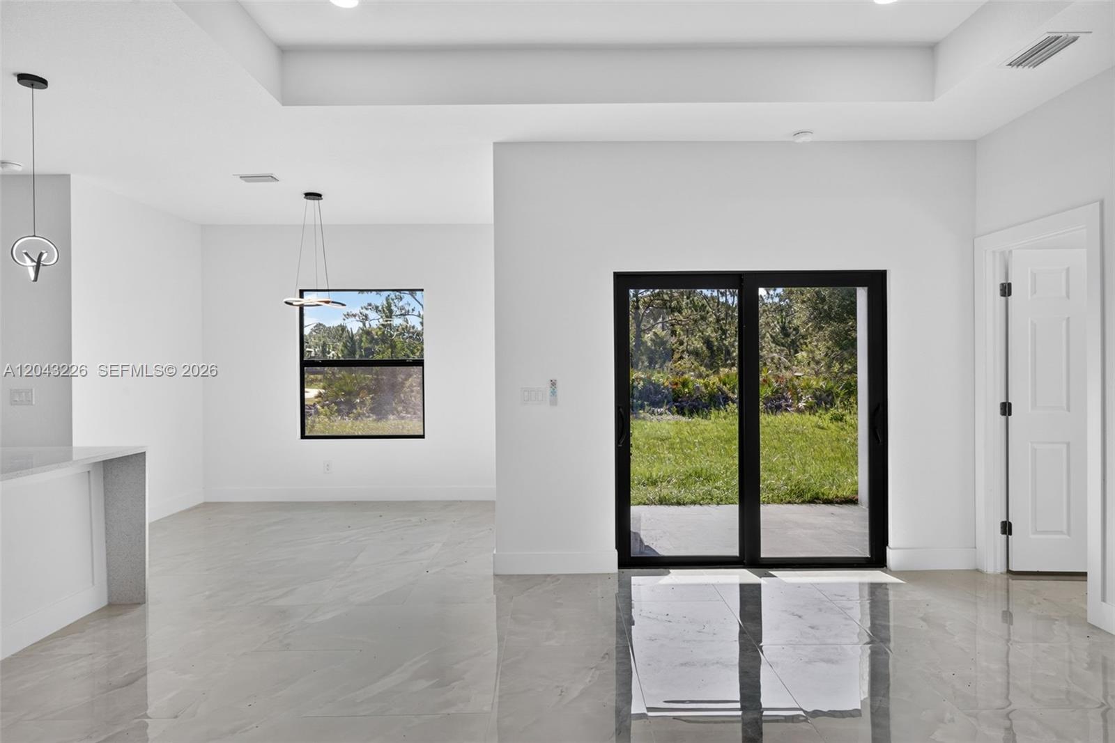 A bright room features white walls, glossy tile floors, a sliding glass door, and windows — 3706 N Gene Ave, Lehigh Acres FL 33971, LEHIGH ACRES, FL