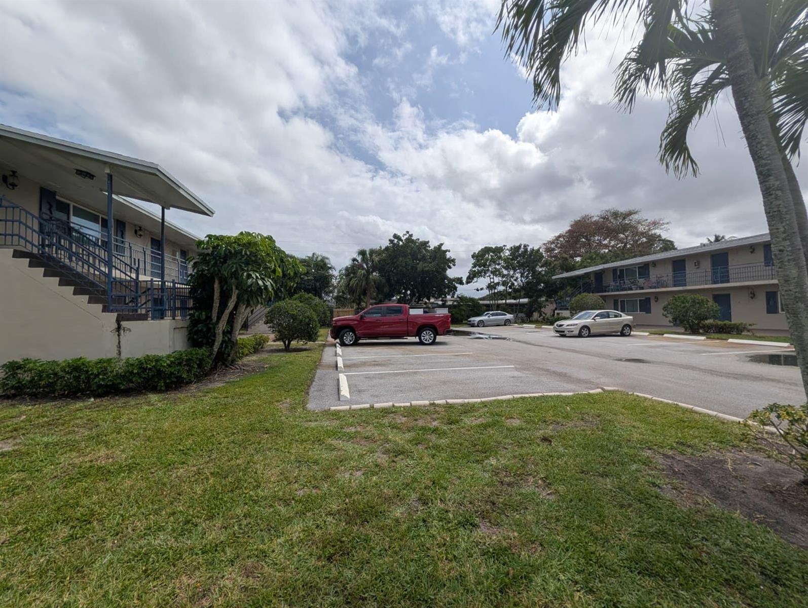 An exterior view of a two-story apartment complex with a parking lot and lawn — 817 Lighthouse Drive Apt B, North Palm Beach FL 33408, NORTH PALM BEACH, FL