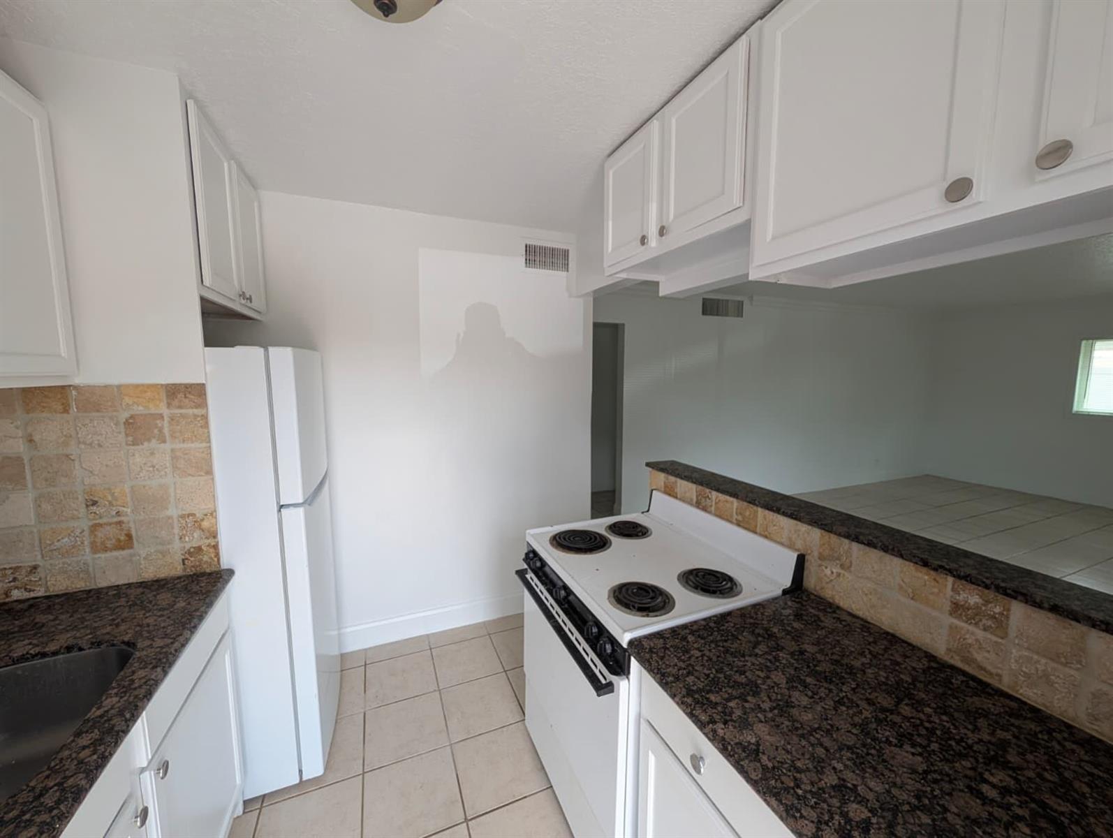 A kitchen features white cabinets, dark granite countertops, a white refrigerator, and a stove — 817 Lighthouse Drive Apt B, North Palm Beach FL 33408, NORTH PALM BEACH, FL