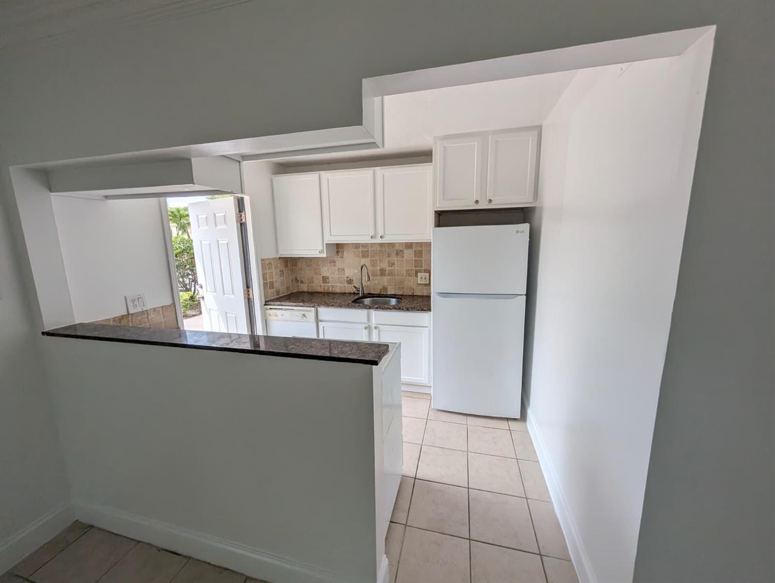 A kitchen with white cabinets, granite countertops, and a tile backsplash viewed from an opening — 817 Lighthouse Drive Apt B, North Palm Beach FL 33408, NORTH PALM BEACH, FL