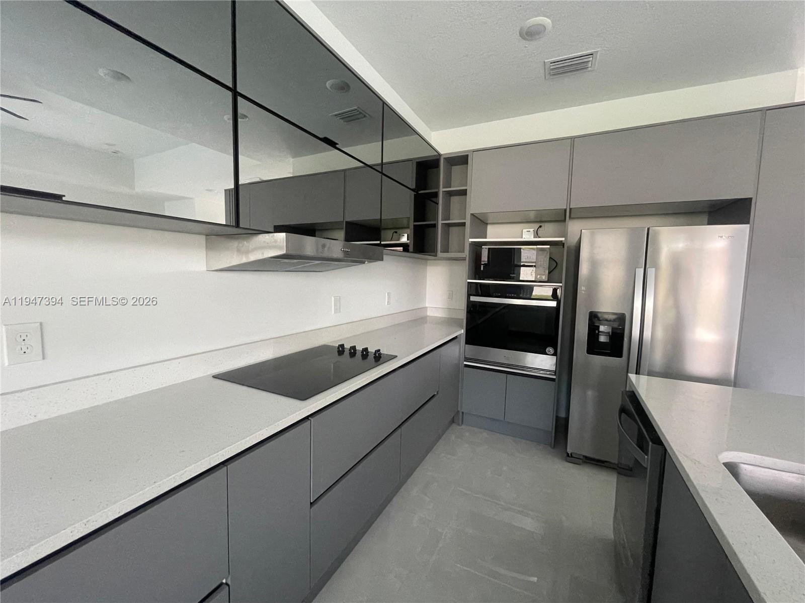 A modern kitchen features gray flat-panel cabinetry, stainless steel appliances, and light quartz countertops — 1326 SEQUOIA RD, Palm Bay FL 32907, PALM BAY, FL