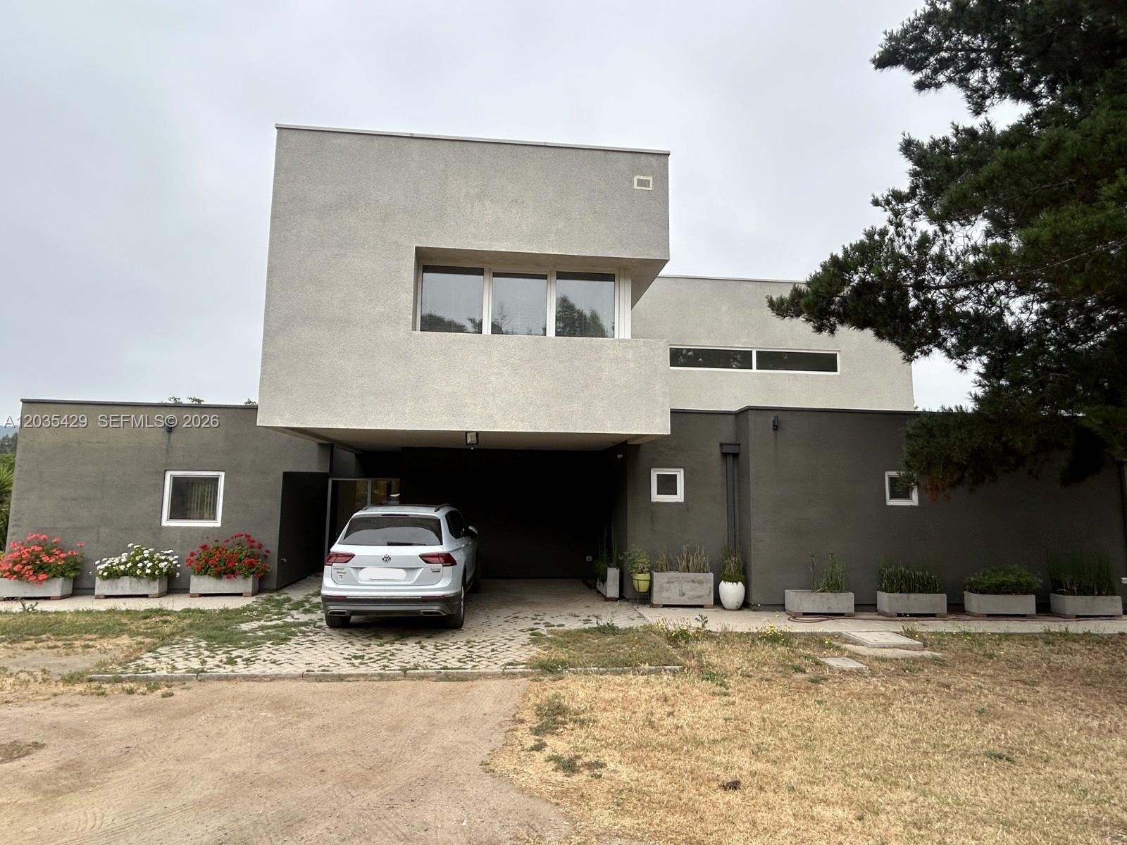 A two-story modern house with a gray exterior, a covered parking area, and several planters — Parcela 12 A Los Molles, OC, OC