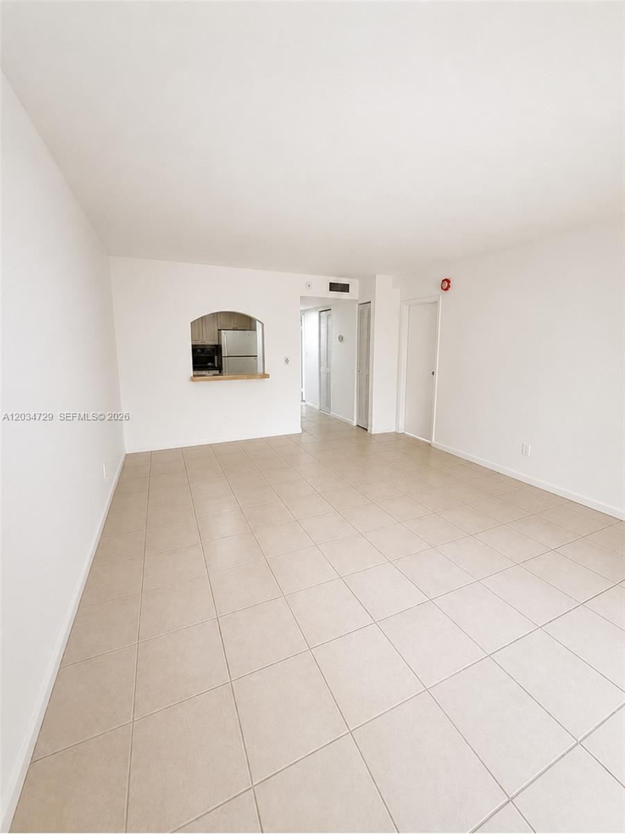 An empty room features light-colored tile flooring, white walls, and a kitchen pass-through window — 13499 Biscayne Blvd # 504, North Miami FL 33181, NORTH MIAMI, FL