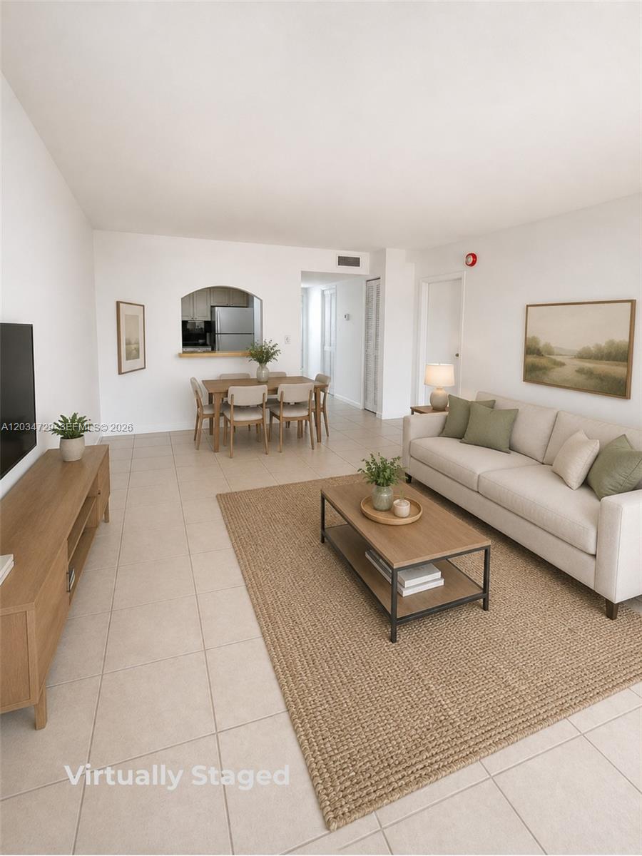 This virtually staged living and dining area features white walls and light-colored tile flooring — 13499 Biscayne Blvd # 504, North Miami FL 33181, NORTH MIAMI, FL