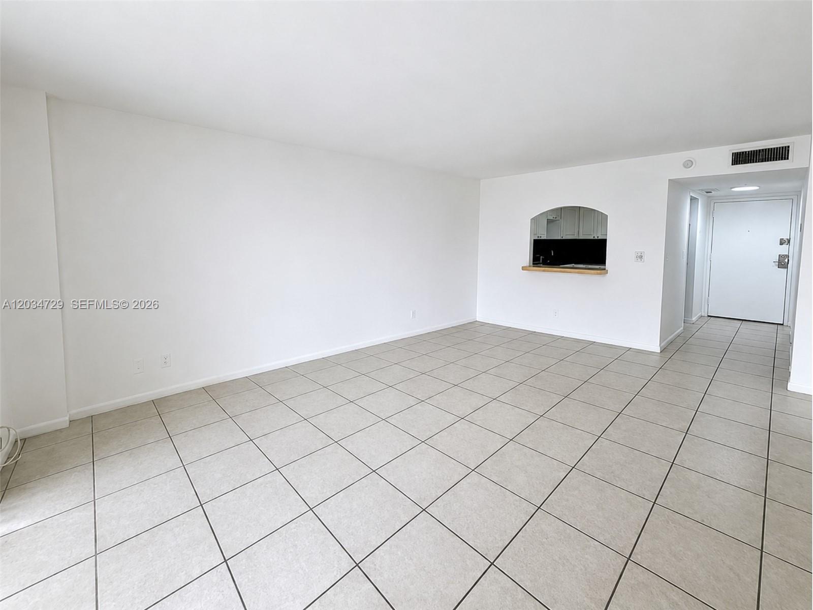 An empty living room features white walls, light-colored tile flooring, and a kitchen pass-through window — 13499 Biscayne Blvd # 504, North Miami FL 33181, NORTH MIAMI, FL