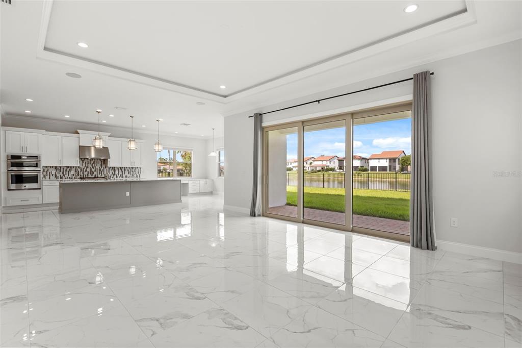 A bright open-concept kitchen and living area with white marble-look tile floors and sliding doors — 10511 ROYAL CYPRESS WAY, ORLANDO, FL