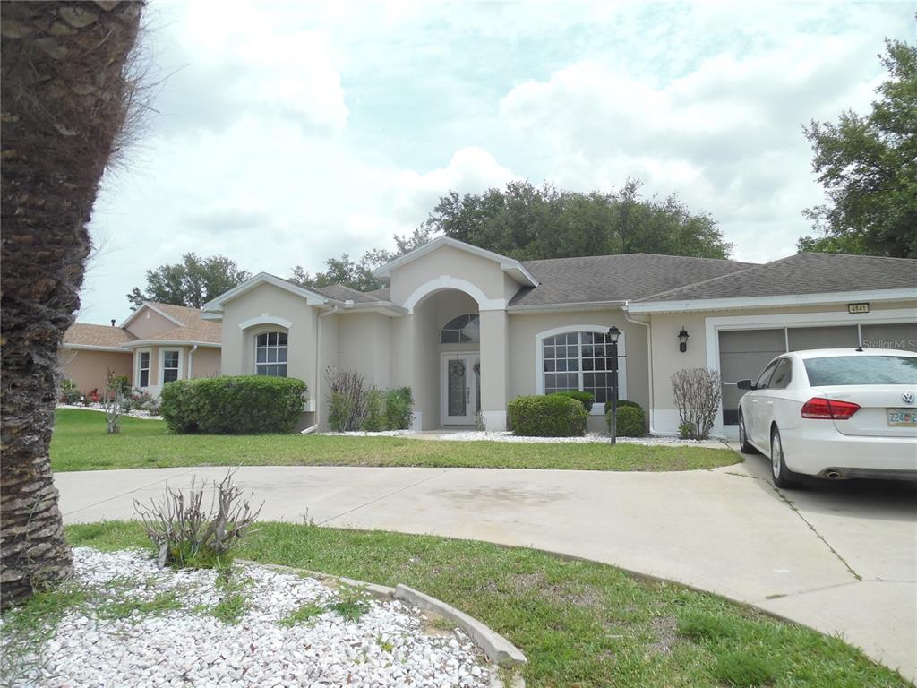 A beige single-story house with a white arched entryway and a concrete driveway — 4841 GLEN COE STREET, LEESBURG, FL