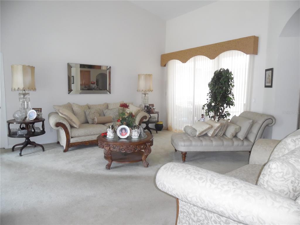 A living room features a sofa, a chaise lounge, a coffee table, and tall windows — 4841 GLEN COE STREET, LEESBURG, FL