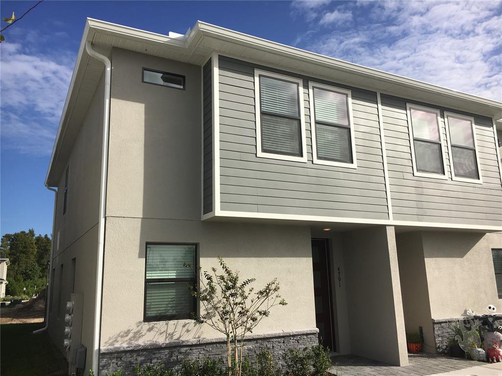 A two-story townhouse exterior features gray horizontal siding, beige stucco, and a stone veneer base — 4791 TERRA ESMERALDA DRIVE, KISSIMMEE, FL