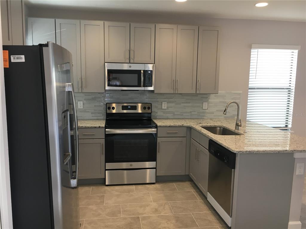 A kitchen with gray cabinets, stainless steel appliances, granite countertops, and a tile backsplash — 4791 TERRA ESMERALDA DRIVE, KISSIMMEE, FL