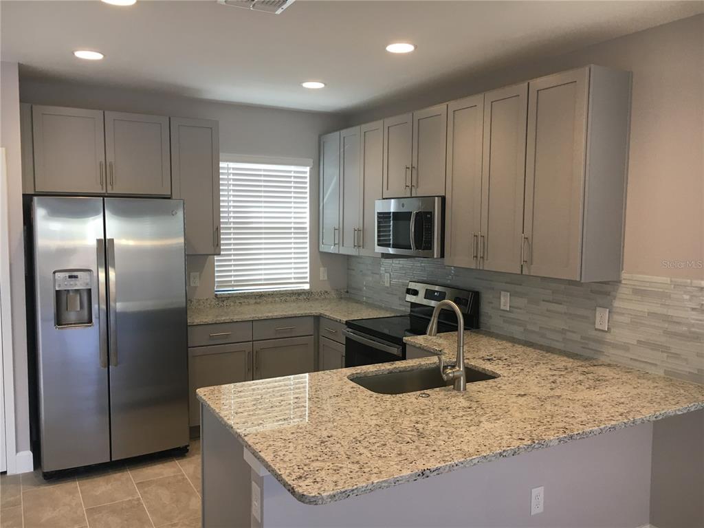 A kitchen with gray cabinets, granite countertops, stainless steel appliances, and a tiled backsplash — 4791 TERRA ESMERALDA DRIVE, KISSIMMEE, FL