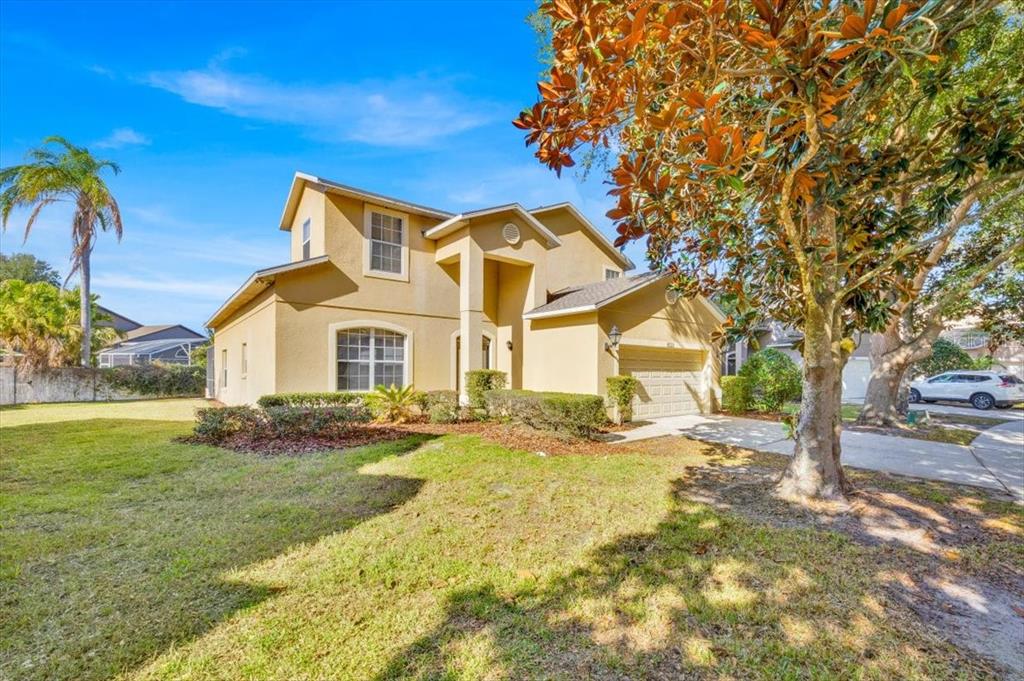 A two-story tan stucco house features a front-facing garage and a large tree nearby — 8023 ACADIA ESTATES COURT, KISSIMMEE, FL
