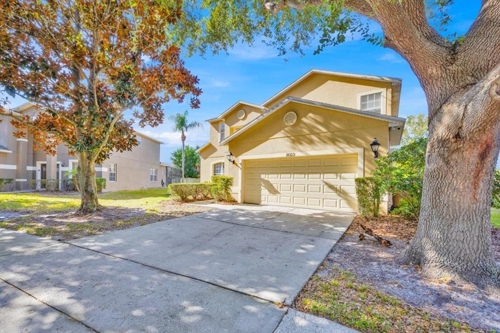 A two-story yellow stucco house features a two-car garage and a large oak tree — 8023 ACADIA ESTATES COURT, KISSIMMEE, FL