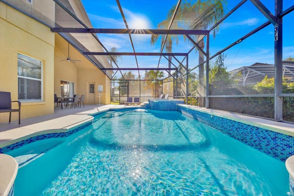 A screened-in swimming pool and spa area with blue tile accents and patio furniture — 8023 ACADIA ESTATES COURT, KISSIMMEE, FL