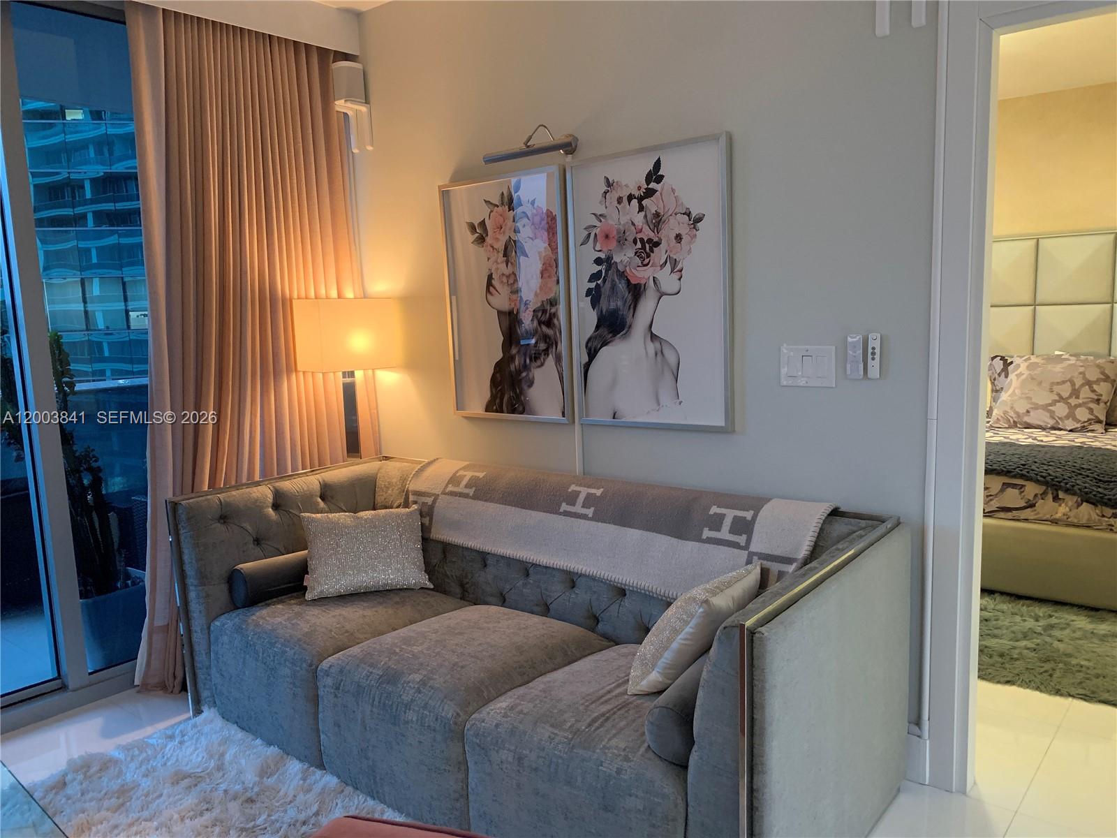 A gray tufted sofa sits in a living room with floral art and pink curtains — 200 Biscayne Boulevard Way # 4011, Miami FL 33131, MIAMI, FL