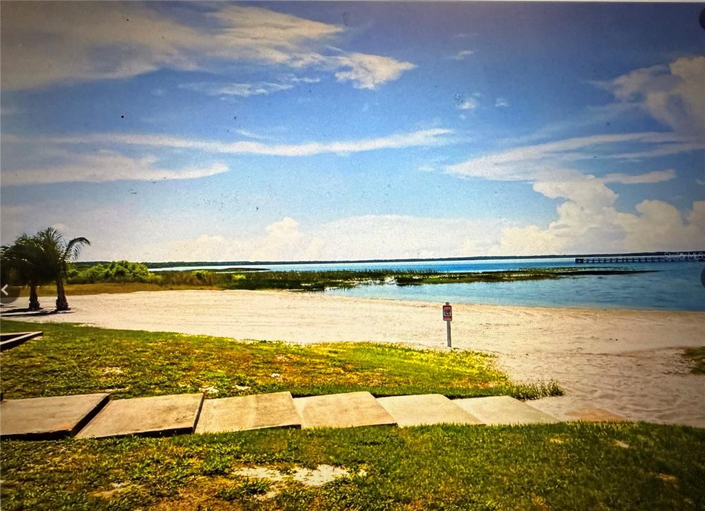 A sandy beach area leads to a body of water with a distant wooden pier — 513 PALM AVENUE, INDIAN LAKE ESTATES, FL
