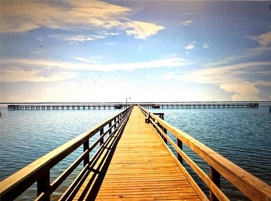 A long wooden pier extends over calm water toward a distant horizon under a cloudy sky — 513 PALM AVENUE, INDIAN LAKE ESTATES, FL