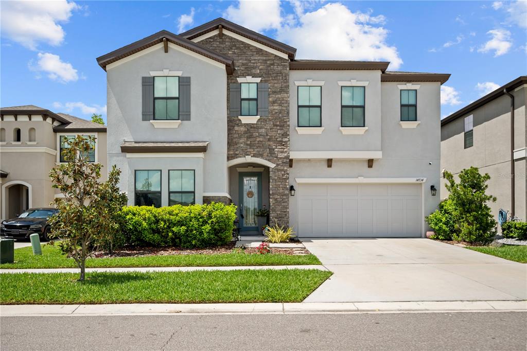 A two-story suburban house features a stone facade, gray stucco, and a two-car garage — 14734 HORSE TROT ROAD, LITHIA, FL