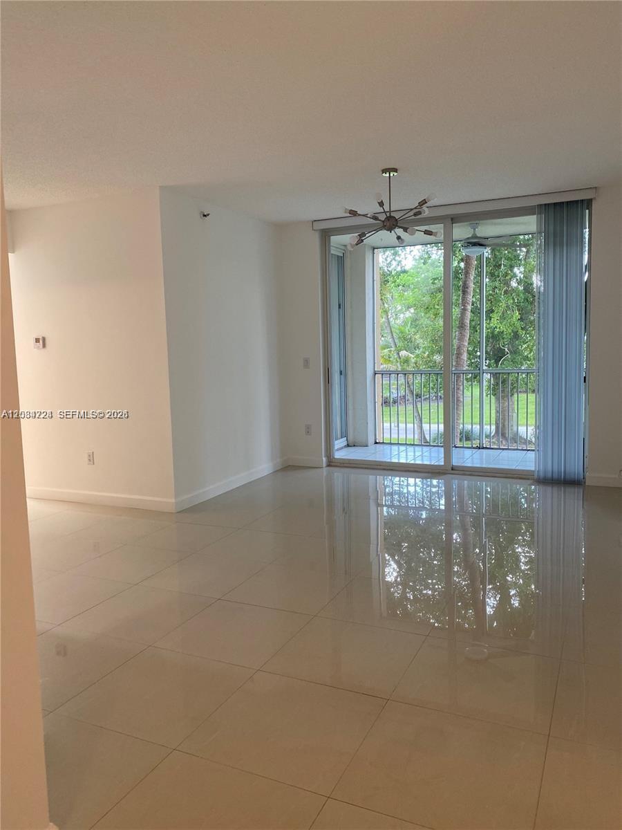 A bright living area features light-colored tile flooring, a modern chandelier, and a sliding glass door — 9805 NW 52nd St # 207, Doral FL 33178, DORAL, FL