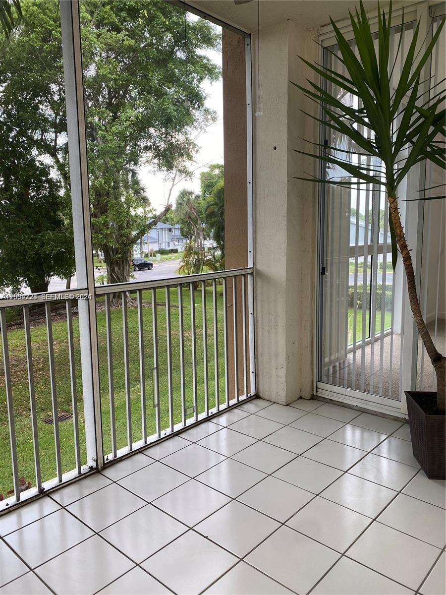 A screened-in balcony with white tile flooring overlooks a grassy area and trees — 9805 NW 52nd St # 207, Doral FL 33178, DORAL, FL