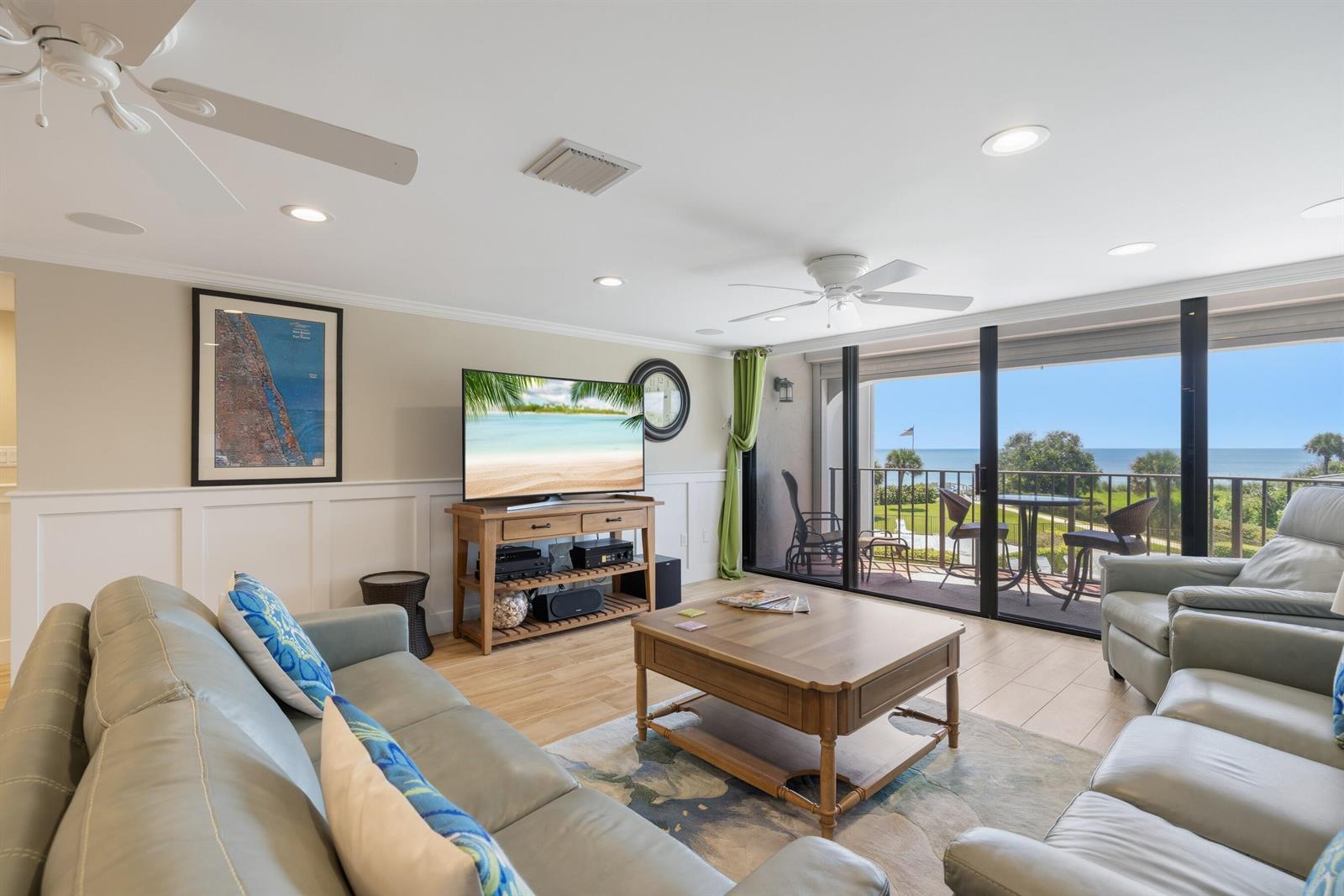 A living room with light wood floors, a television, and a balcony overlooking the ocean — INDIAN RIVER SHORES, FL
