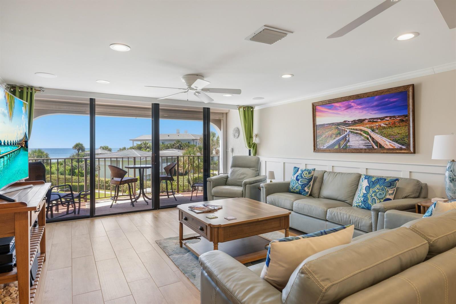 A living room with light wood floors, leather sofas, and a balcony overlooking the ocean — INDIAN RIVER SHORES, FL