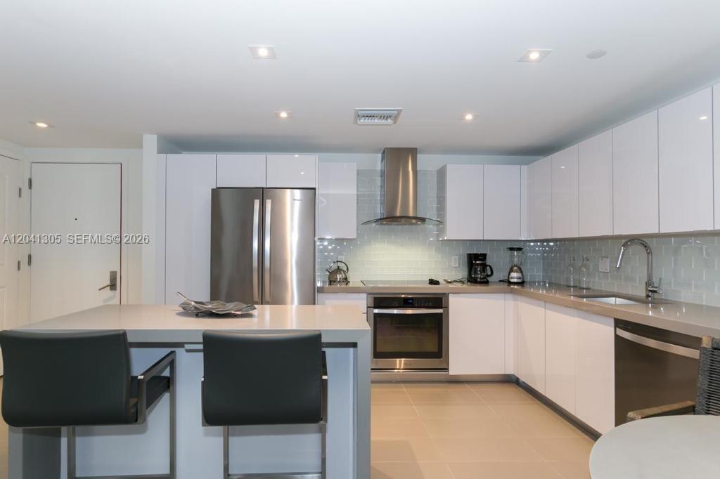 A modern kitchen features white cabinets, stainless steel appliances, and a central island with seating — MIAMI, FL