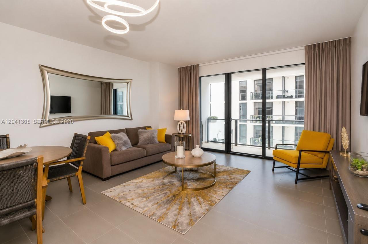 A modern living room features a brown sofa, yellow armchair, and a balcony with city views — MIAMI, FL
