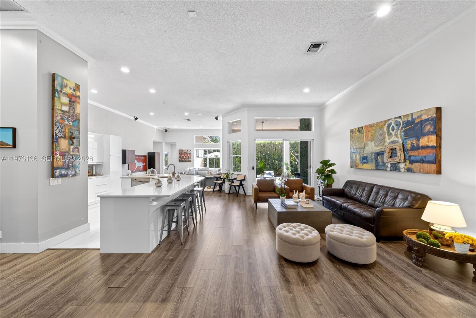 An open-concept living area features a white kitchen island, wood flooring, and a leather sofa — 1623 Blue Jay Cir, Weston FL 33327, WESTON, FL