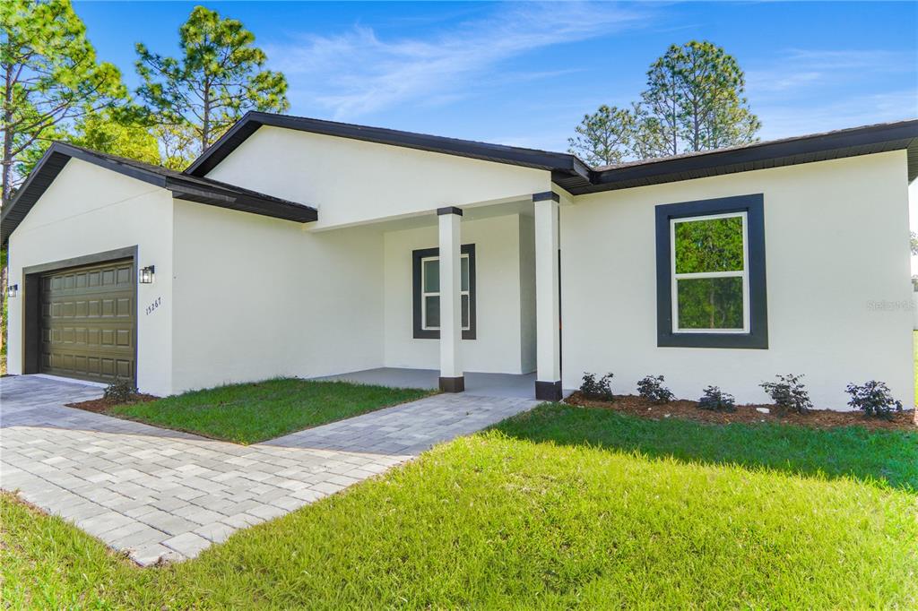 A single-story house with white stucco walls, a dark garage door, and a paved walkway — 15267 SW 50TH COURT ROAD, OCALA, FL