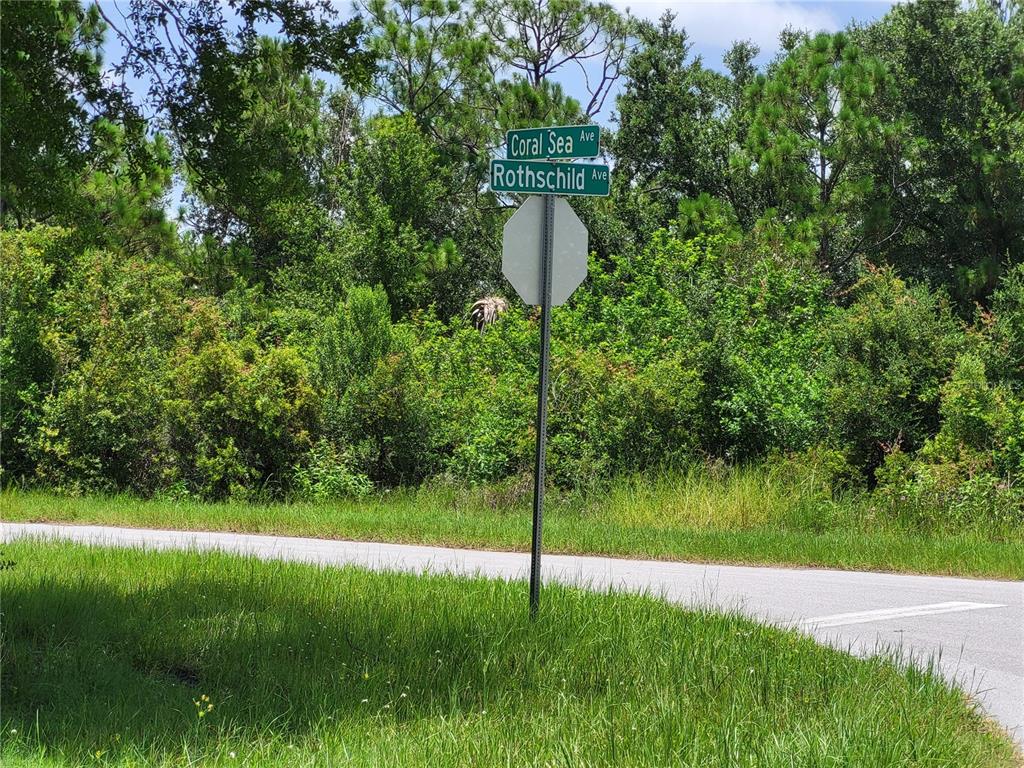 A street sign for Coral Sea Avenue and Rothschild Avenue stands beside a paved road — 14471 CORAL SEA AVENUE, PORT CHARLOTTE, FL