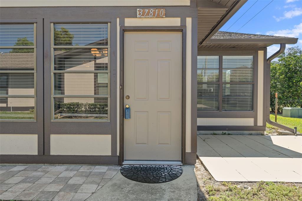 A beige front door with a lockbox sits between two windows on a house exterior — 37810 ALISSA DRIVE, ZEPHYRHILLS, FL