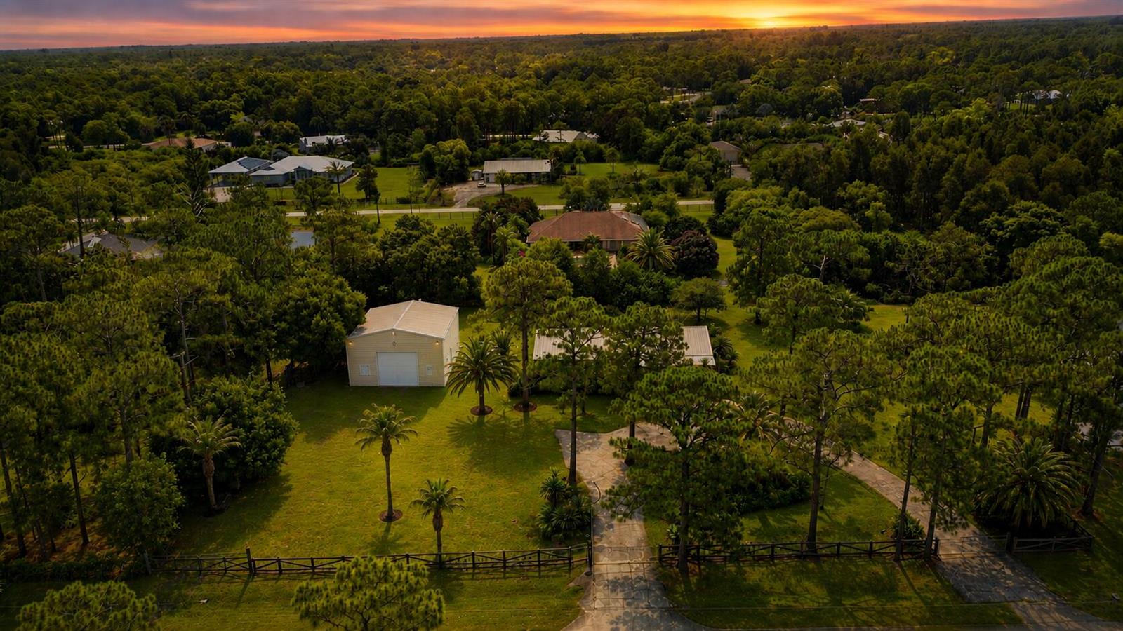 An aerial view shows a house and detached garage surrounded by trees at sunset — 16208 132nd Terrace N, Jupiter FL 33478, JUPITER, FL