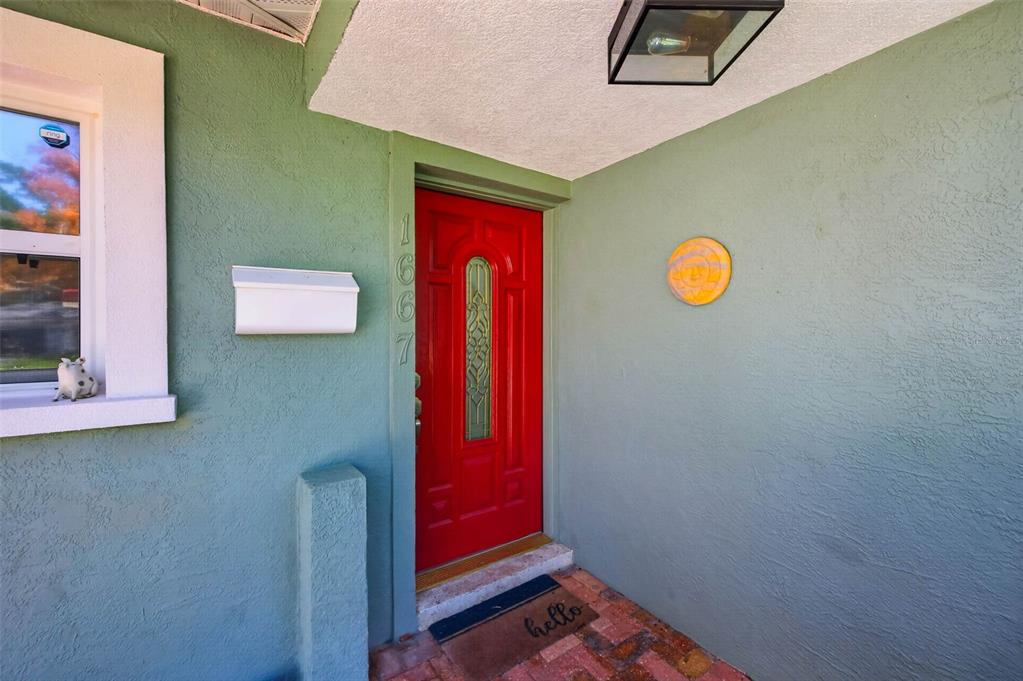 A red front door with a glass insert is set into a teal exterior wall — 1667 N DAKOTA AVENUE NE, ST PETERSBURG, FL