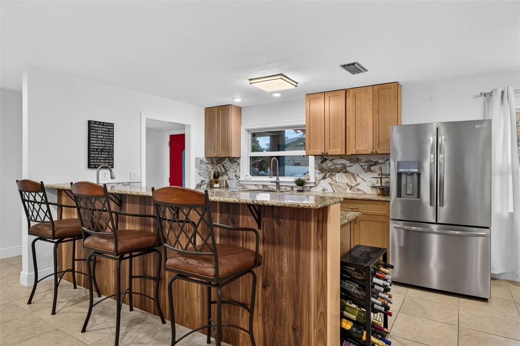 A kitchen features wood cabinets, granite countertops, a breakfast bar with stools, and stainless appliances — 1667 N DAKOTA AVENUE NE, ST PETERSBURG, FL