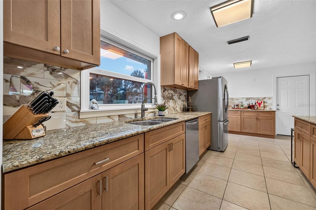 A kitchen features light wood cabinets, granite countertops, a stainless steel refrigerator, and tile flooring — 1667 N DAKOTA AVENUE NE, ST PETERSBURG, FL