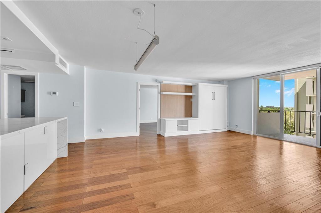 An open living area features hardwood floors, a white built-in wall unit, and a balcony — 1900 S Ocean Boulevard Apt 6j, Pompano Beach FL 33062, POMPANO BEACH, FL