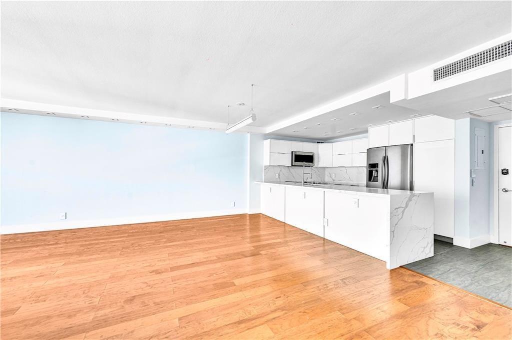 A modern kitchen with white cabinetry and marble countertops opens into a spacious living area — 1900 S Ocean Boulevard Apt 6j, Pompano Beach FL 33062, POMPANO BEACH, FL