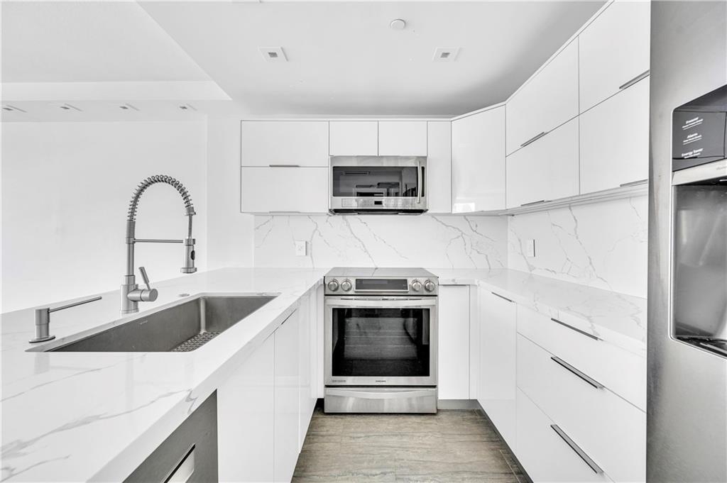 A modern kitchen features white glossy cabinets, stainless steel appliances, and white marble-patterned countertops — 1900 S Ocean Boulevard Apt 6j, Pompano Beach FL 33062, POMPANO BEACH, FL
