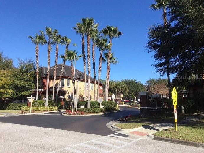 A gated entrance features tall palm trees and a multi-story building under a clear sky — 2141 PORTOFINO PLACE UNIT 8-2826, PALM HARBOR, FL