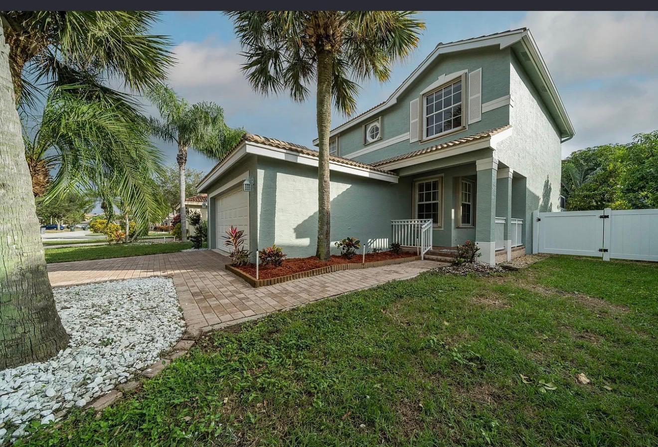 A two-story house with green stucco siding, a paved driveway, and a palm tree — 5144 Aurora Lake Circle, FL 33463, FL