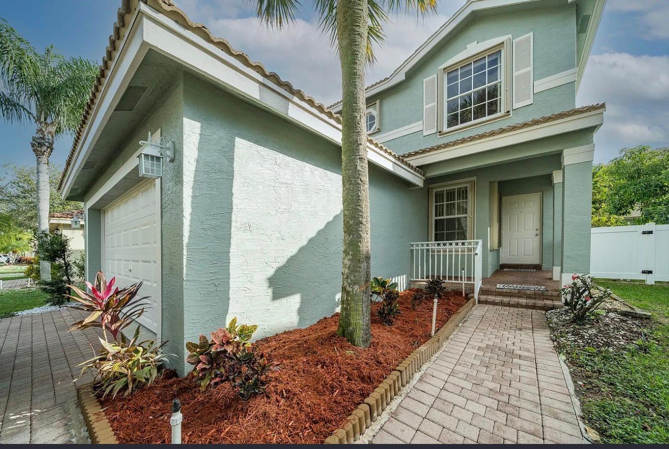 A light green two-story house with a brick walkway, mulch garden, and attached garage — 5144 Aurora Lake Circle, FL 33463, FL