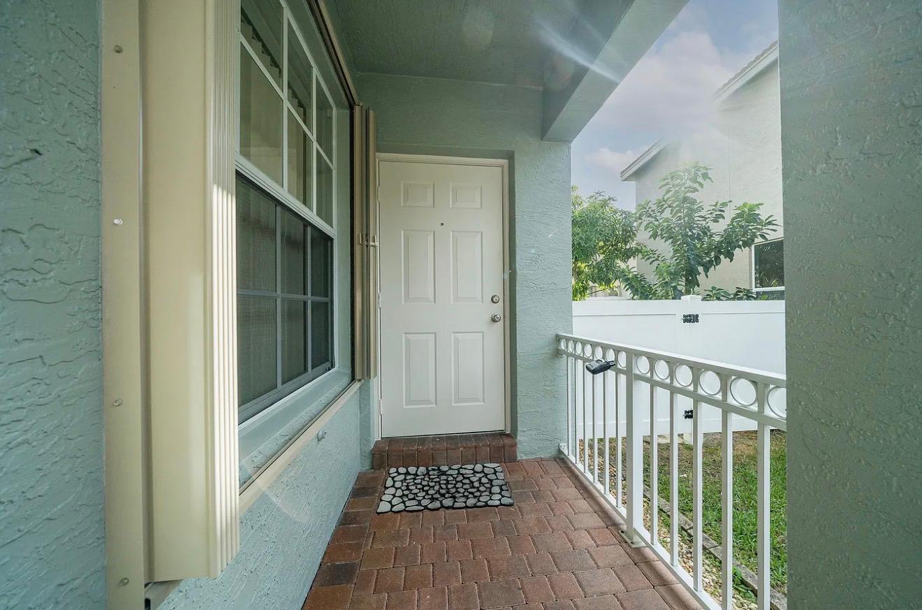 A covered entryway features a white front door, brick flooring, and a white metal railing — 5144 Aurora Lake Circle, FL 33463, FL