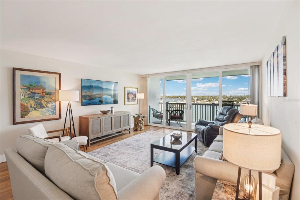 A living room features a sofa, armchairs, a television, and large sliding doors overlooking water — 500 TREASURE ISLAND CAUSEWAY UNIT 711, TREASURE ISLAND, FL