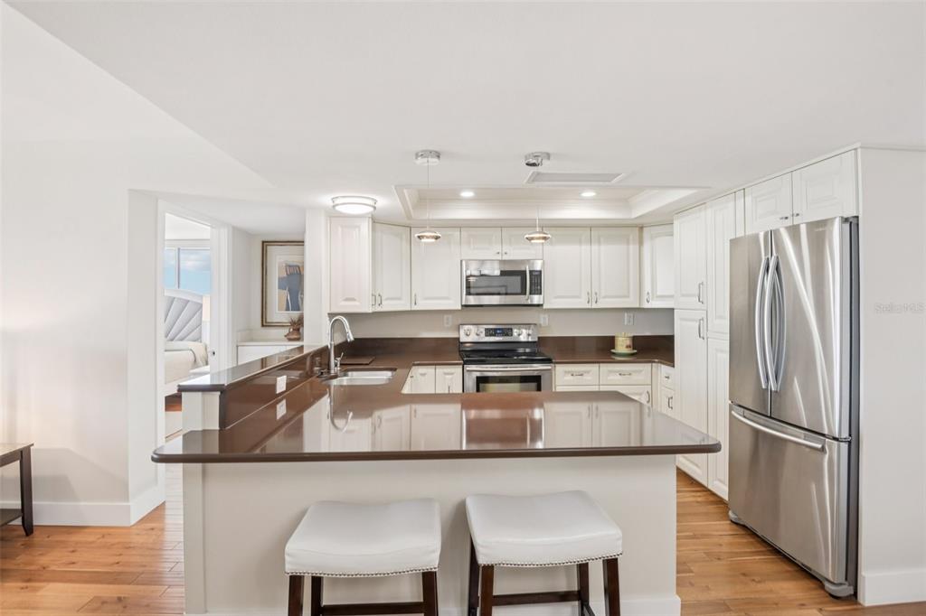 A kitchen with white cabinets, brown countertops, stainless steel appliances, and two bar stools — 500 TREASURE ISLAND CAUSEWAY UNIT 711, TREASURE ISLAND, FL